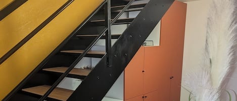 Un escalier avec une rampe en métal noir, des marches en bois et un mur jaune.