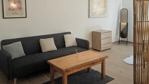 Un soggiorno moderno con un divano grigio scuro, un tavolino in legno e un tappeto nero. Si notano due quadri appesi, uno specchio e un mobiletto in legno.