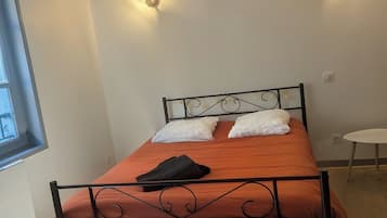 Una cama individual con estructura metálica, un edredón naranja y dos almohadas blancas. Hay dos lámparas de pared a cada lado de la cama.