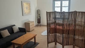 Un salon comprenant un canapé, une table basse en bois, un miroir, une cloison en bois et une fenêtre donnant sur un paysage agréable.