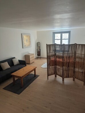 Una sala de estar con sofá, una mesa de centro de madera, un espejo, un panel divisor de madera y una ventana con vistas.