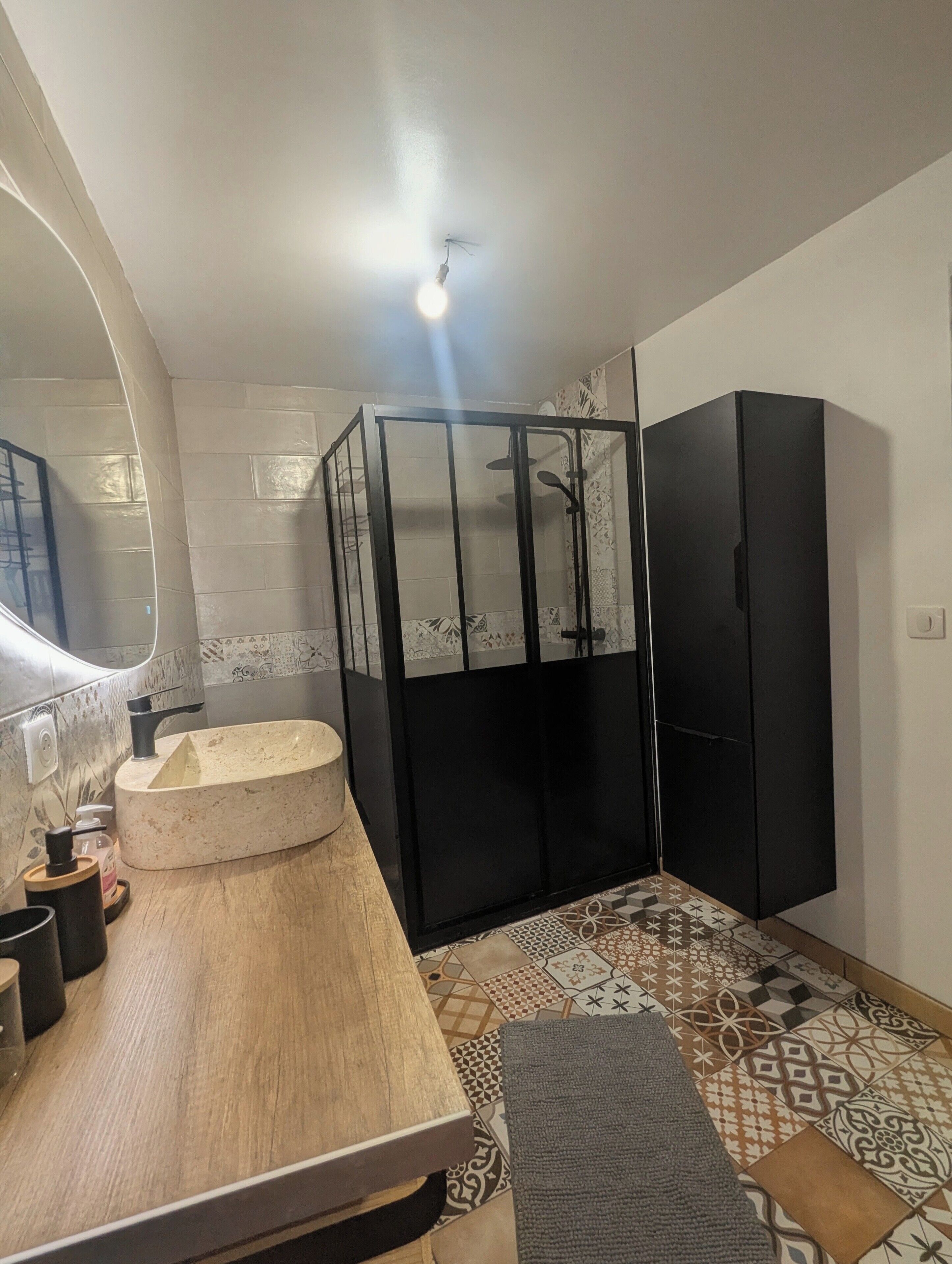 Un baño con tocador de madera, cabina de ducha de vidrio y armario negro.