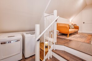 A laundry area with two white appliances, a wooden staircase leading to a living room with a brown sofa and a patterned rug. -  2-bedroom guest house in Upstate, SC (Easley)