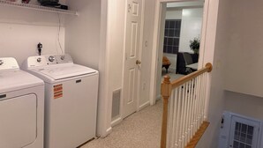 A laundry room with two front-loading washing machines, a white door, and a wooden staircase railing. - 2 bedroom furnished townhome, washer & dryer, Central Air, Wifi & New appliances (Atlanta)