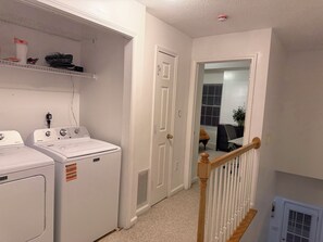 A laundry room with two front-loading washing machines, a white door, and a wooden staircase railing. - 2 bedroom furnished townhome, washer & dryer, Central Air, Wifi & New appliances (Atlanta)