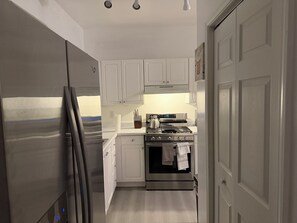A compact kitchen with white cabinets, a stainless steel refrigerator, a stove, and a dishwasher. - 2 bedroom furnished townhome, washer & dryer, Central Air, Wifi & New appliances (Atlanta)