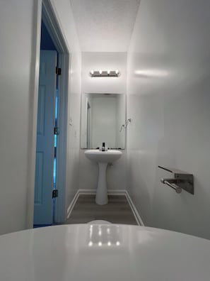 Ein Badezimmer mit einem weißen Waschbecken, einem Spiegel darüber und einer Tür zu einem anderen Raum.