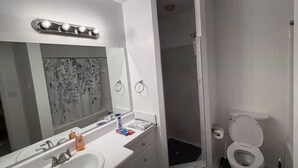 A modern bathroom with a large mirror, a sink, a shower enclosure, and a toilet. - 2 bedroom furnished townhome, washer & dryer, Central Air, Wifi & New appliances (Atlanta)