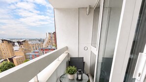 Un balcon avec une petite table et des chaises, un pot de fleurs et une vue sur le paysage urbain.