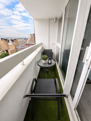 A balcony with a small table and chairs, a potted plant, and a view of the cityscape. - Canary Wharf Apartment with Balcony, Workspace & Parking (London)