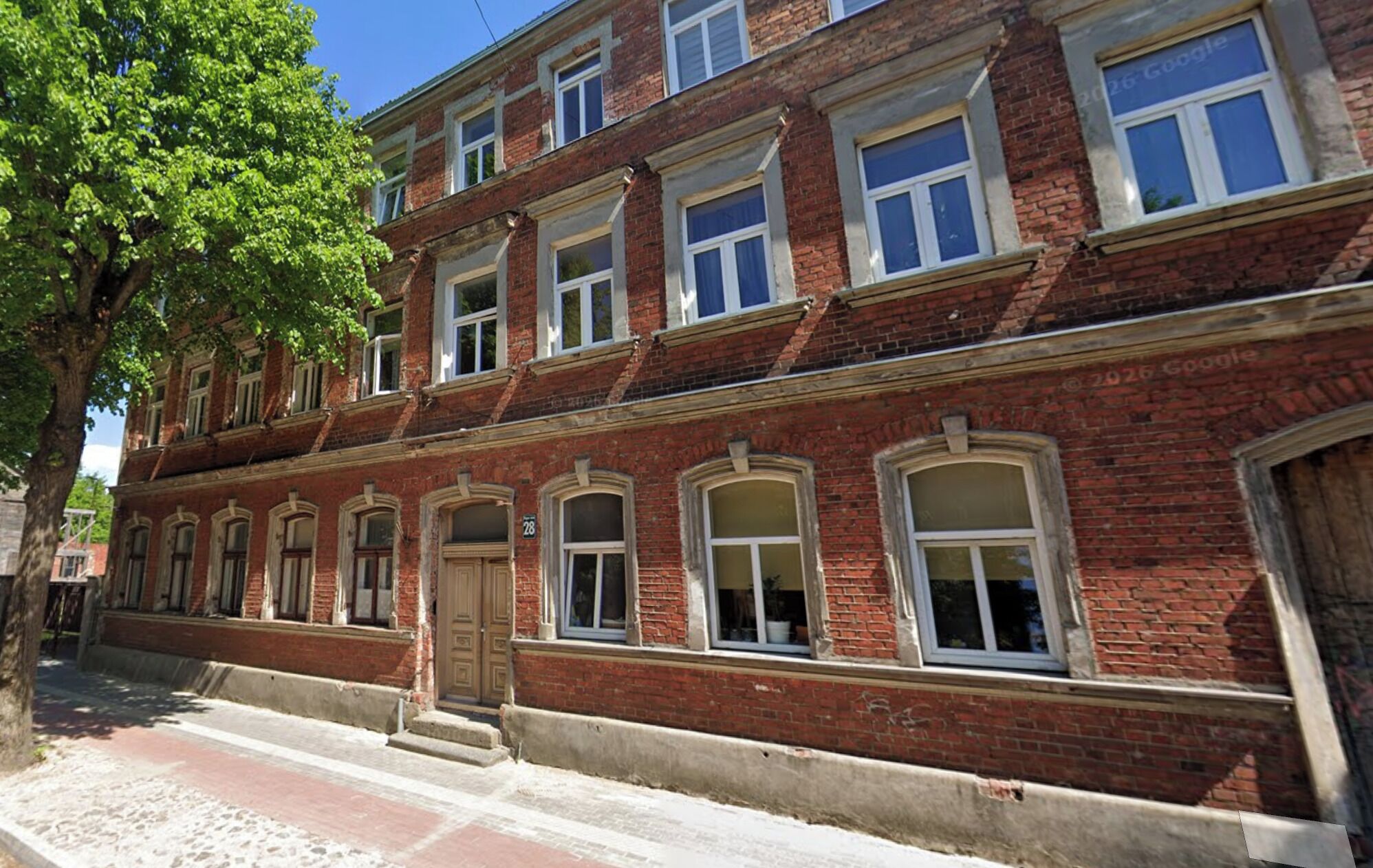 Ein mehrgeschossiges Backsteingebäude mit einer symmetrischen Fassade, großen Fenstern und einem zentralen Eingang.