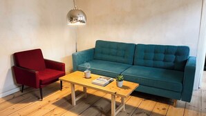 Et værelse med en rød stol, en søgrøn sofa, et træbord med en bog og en plante, samt en pendellampe.
