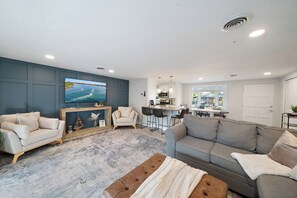 Ein modernes Wohnzimmer mit Flachbildfernseher, einer Couch, einem Couchtisch und einer Küchenzeile im Hintergrund.