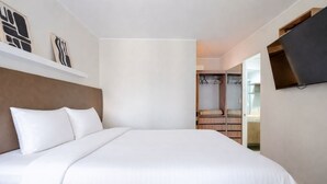 Ett hotellrum med en stor säng, en garderob och en tv som är monterad på väggen.