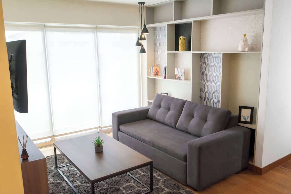 A modern living room with a grey sofa, a coffee table, and a bookshelf.