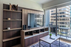 Een moderne woonkamer met een flatscreen televisie, houten planken, een kleine tafel en een balkon met uitzicht op een hoog gebouw.