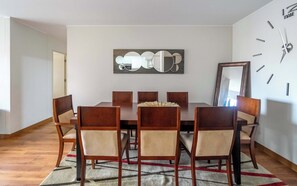 Ein Esszimmer mit einem großen Tisch, sechs Stühlen, einem Teppich, einer Wanduhr und einem Spiegel.