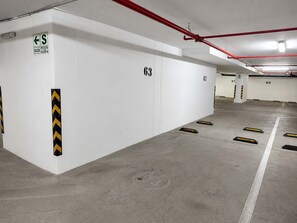 Een parkeergarage met witte muren, genummerde parkeerplaatsen en vluchtwegwijzers.