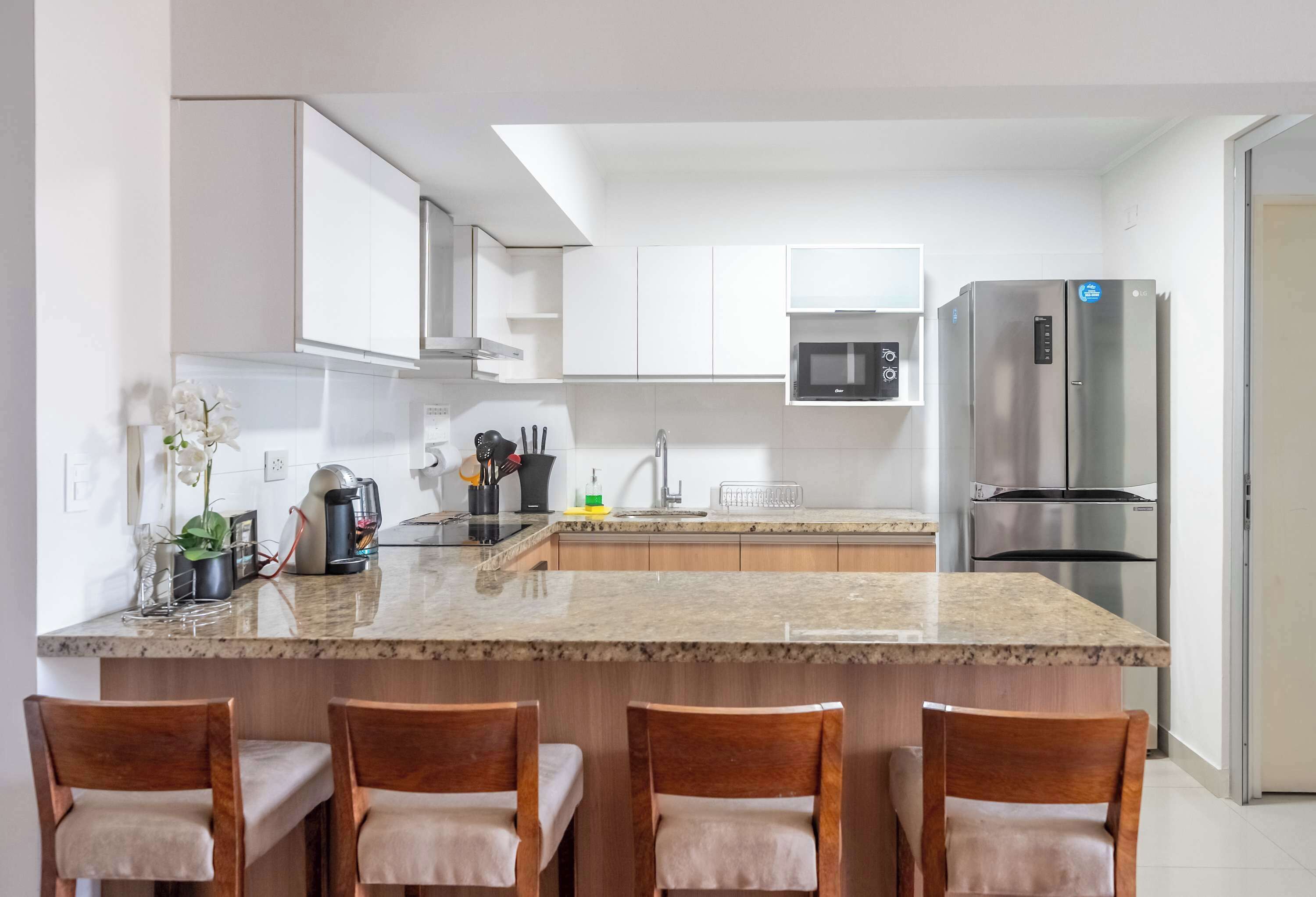 A modern kitchen with white cabinets, a granite countertop, a stainless steel refrigerator, and a built-in microwave.