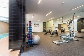 Ein modernes Fitnessstudio mit unterschiedlichen Trainingsgeräten, einem großen Spiegel und einer Wand mit der Aufschrift 'FOCUS'.