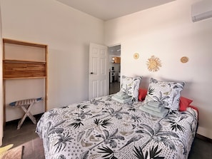 A bedroom with a bed, a wooden shelf, and a door leading to a kitchen. - KOE HOUSE RAIATEA - FARE MATAHERE - View of Bora Bora & Sunsets (Tevaitoa)
