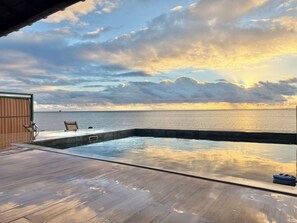 En træterrasse med swimmingpool, udsigt over vand og solnedgang.