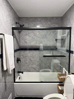 Un baño moderno con ducha de vidrio, bañera blanca y retrete.