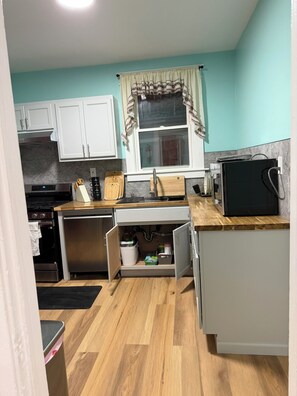 A compact kitchen with white cabinets, a microwave, a stove, and a window with curtains. - MRSP 07 Luxury Family Home Near Niagara Falls (Niagara Falls)