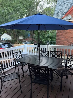 Una terraza con mesa y sillas, una sombrilla azul y una barandilla blanca.