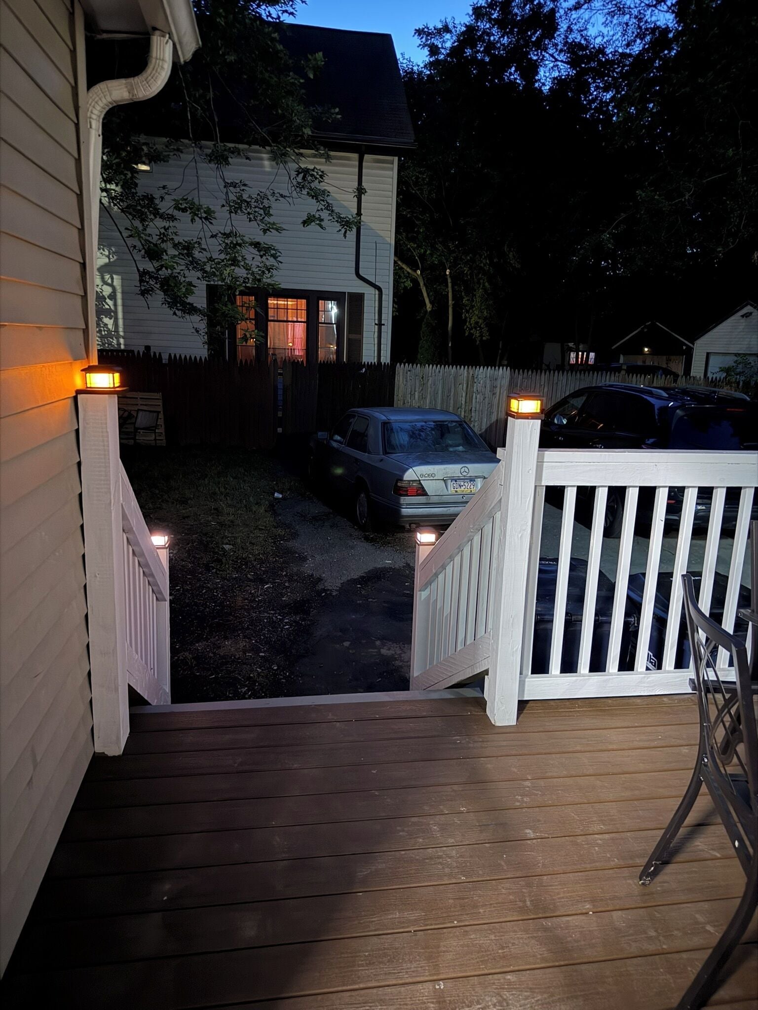 A wooden deck leading to a house with a fenced yard, a parked car, and a visible garage door.