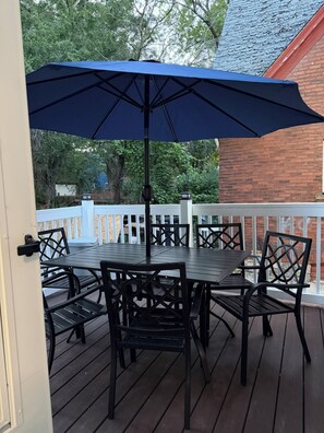 Una terraza con mesa y sillas, un paraguas azul y un muro de ladrillo al fondo.