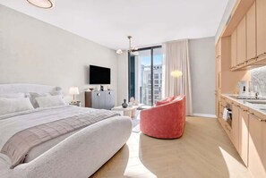 Ein modernes Hotelzimmer mit einem großen Bett, einem roten Sessel, einem Flachbildfernseher, einem Schreibtisch und Blick auf die Stadt.