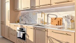 Una cocina moderna con armarios de madera clara, encimera de mármol, horno empotrado y pileta de acero inoxidable.