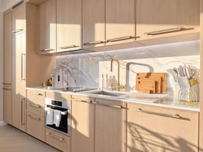 Eine moderne Küche mit hellen Holzschränken, einer Marmorarbeitsplatte, einem eingebauten Ofen und einer Edelstahlspüle.