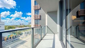 Un balcón moderno con barandillas de vidrio, vista despejada de la calle y un edificio con balcones.