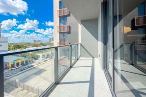 A modern balcony with glass railings, a clear view of the street below, and a building with balconies.