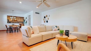 A modern living room with a sectional sofa, a round coffee table, and a dining area with chairs and a table. - 2BR Condo w/ Pool, BBQ, Parking | Beach & Galleria (Fort Lauderdale)