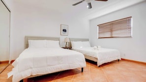 A hotel room with two beds, a ceiling fan, a window with blinds, and a framed picture on the wall. - 2BR Condo w/ Pool, BBQ, Parking | Beach & Galleria (Fort Lauderdale)
