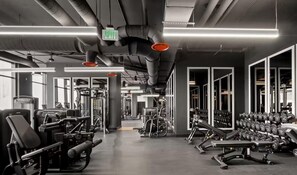 A gym with exercise equipment, weight racks, and a clear exit sign. - Luxury Studio | Prime Downtown Views (Miami)