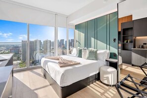 A modern bedroom with a large bed, a bedside table, a chair, and a view of the city. - Luxury Studio | Prime Downtown Views (Miami)