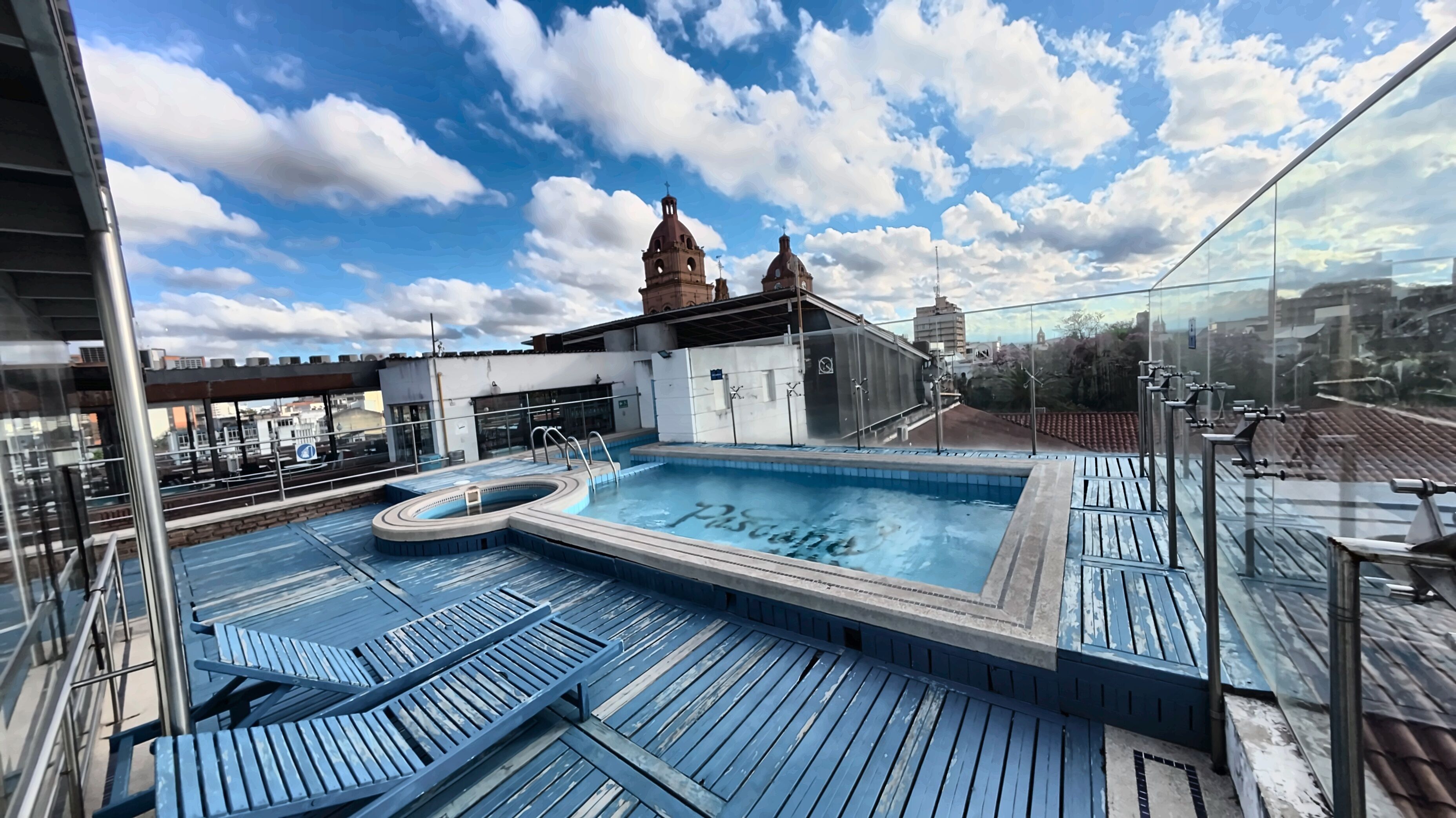 En pool på taget med jacuzzi, omgivet af træterrasse og metalgelændere.