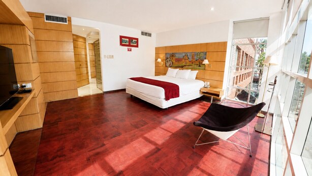 A hotel room with a large bed, a desk with a computer, a chair, and a painting on the wall. - Hotel Pascana centro (Santa Cruz)