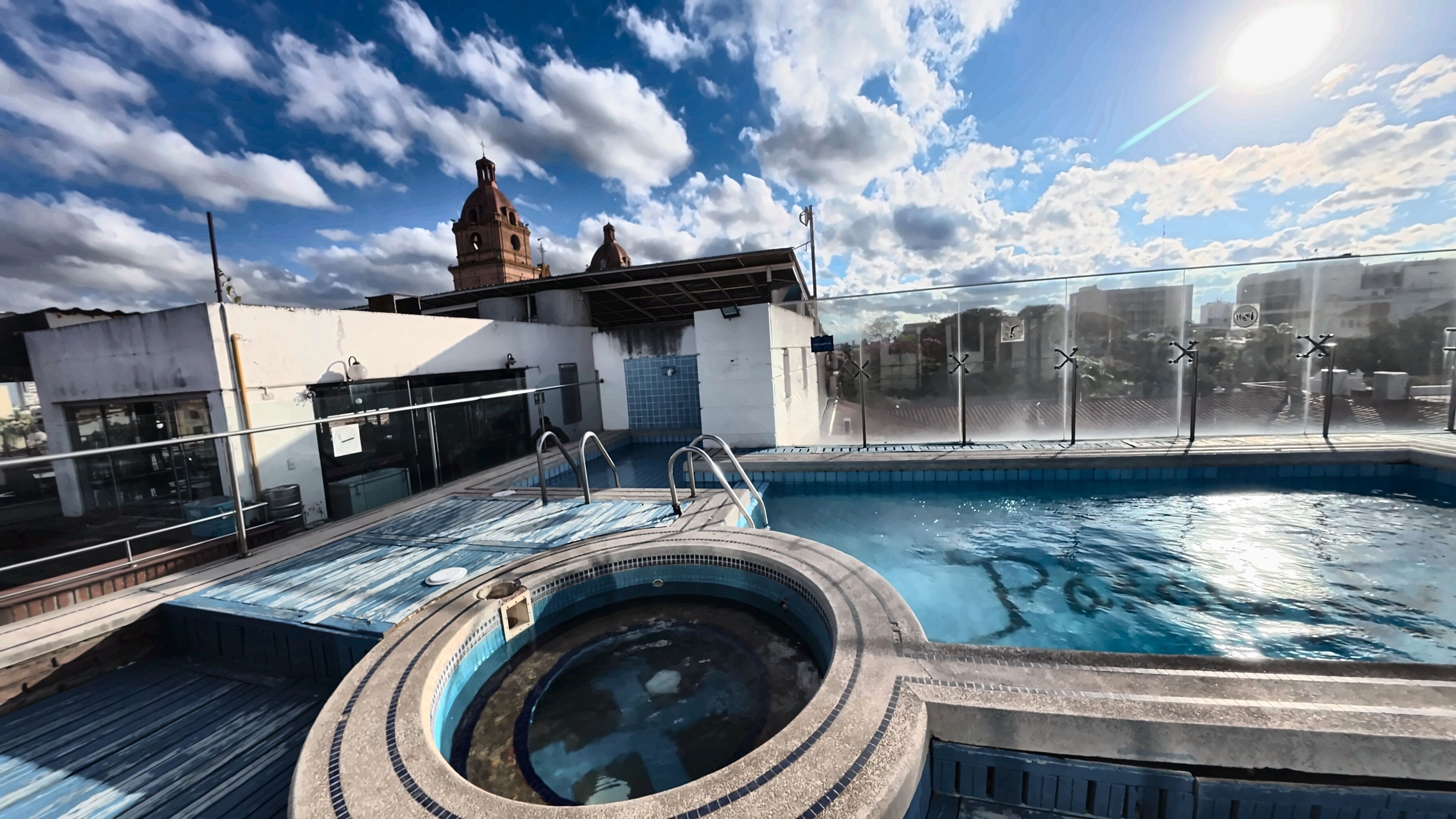 Una piscina en la azotea con un jacuzzi circular, una fuente de agua y vistas a un edificio con una torre del reloj.