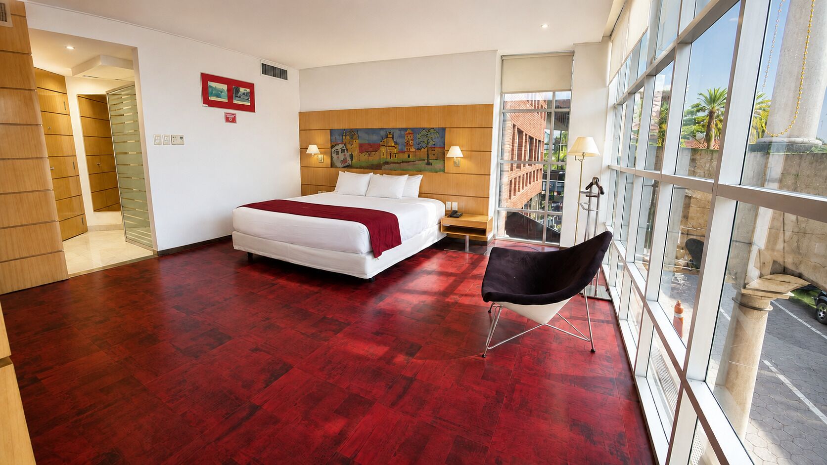 A hotel room with a large bed, a chair, and a view through the window.
