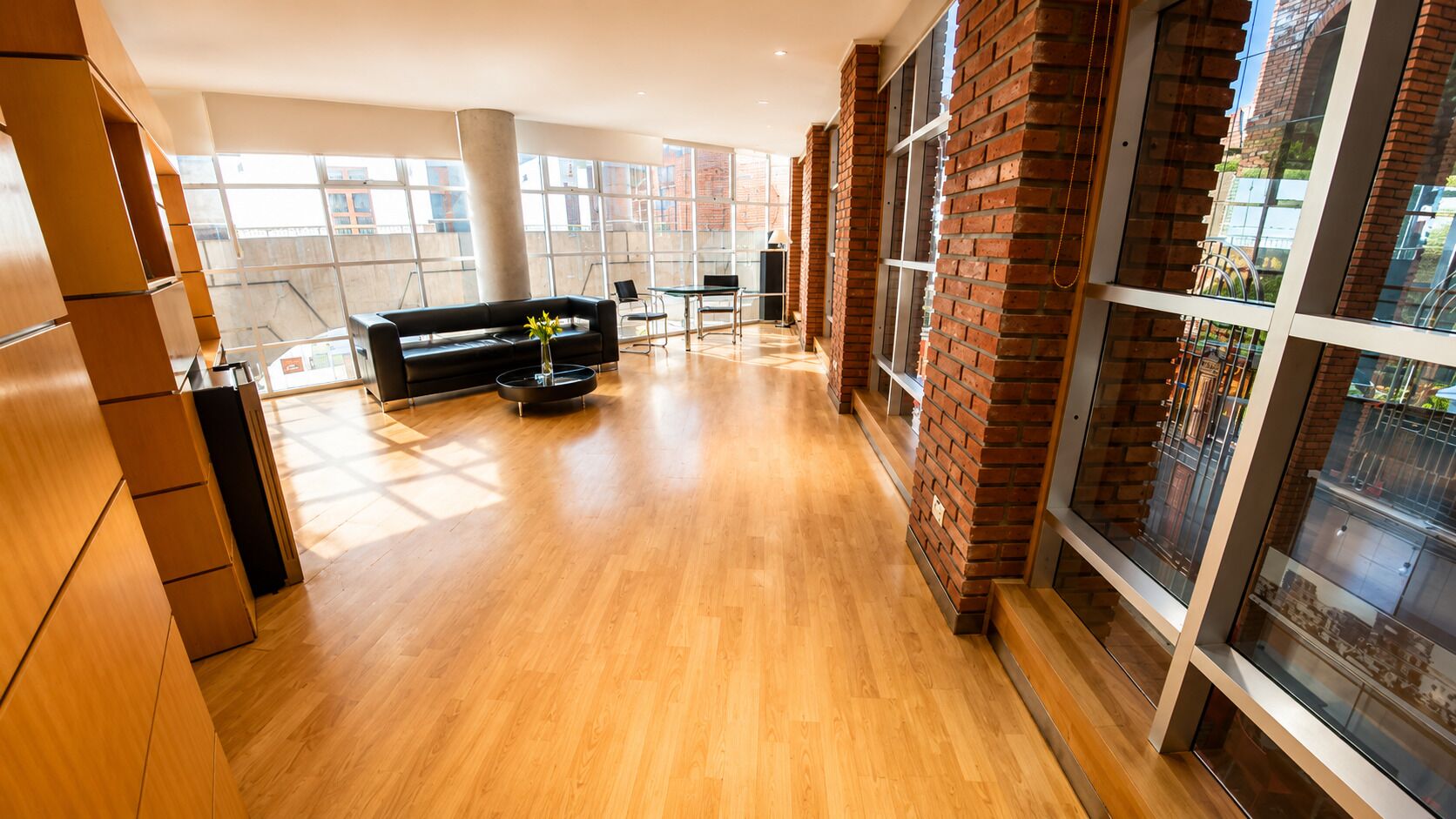 Un interior amplio con suelo de madera, un sofá negro y un jarrón con flores.