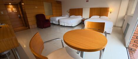 Ein Hotelzimmer mit einem runden Holztisch, zwei Einzelbetten, einem roten Sessel und einer Holzwand.