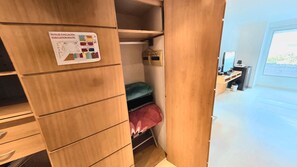 A wooden closet with a sign indicating an evacuation route, a bed with a red cover, and a desk with a computer. - Hotel Pascana centro (Santa Cruz)