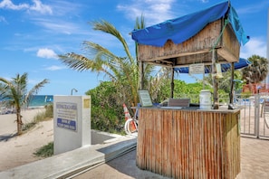 Ein Kiosk am Strand mit blauem Planendach, Schild zur Kennzeichnung von Kartenzahlung und Warnschild vor möglichen Gefahren.