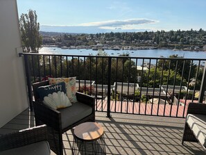 Ein Balkon mit Korbmöbeln, Blick auf eine Marina und eine Stadtlandschaft im Hintergrund.