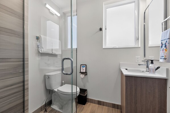 A modern bathroom with a glass shower enclosure, a toilet, a sink with a mirror, and a framed picture on the wall. - Stunning water view, pet friendly, luxury 3-bedroom townhome with AC in Seattle (Seattle)